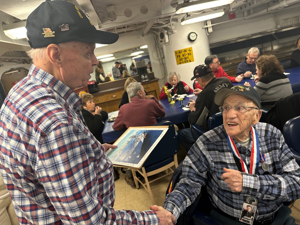John "Johnny Q" Quinesso Sr, a WWII veteran, right, shakes hands with a friend during his 100th birthday celebration on Thursday, Feb. 5, 2026 in Camden, N.J., aboard the Battleship New Jersey. (AP Photo/Tassanee Vejpongsa)