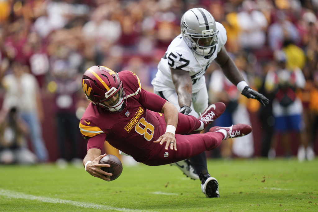Washington Commanders quarterback Marcus Mariota (8) scores a touchdown as Las Vegas Raiders linebacker Germaine Pratt (57) defends during the first half of NFL football game Sunday, Sept. 21, 2025, in Landover, Md. (AP Photo/Stephanie Scarbrough)
