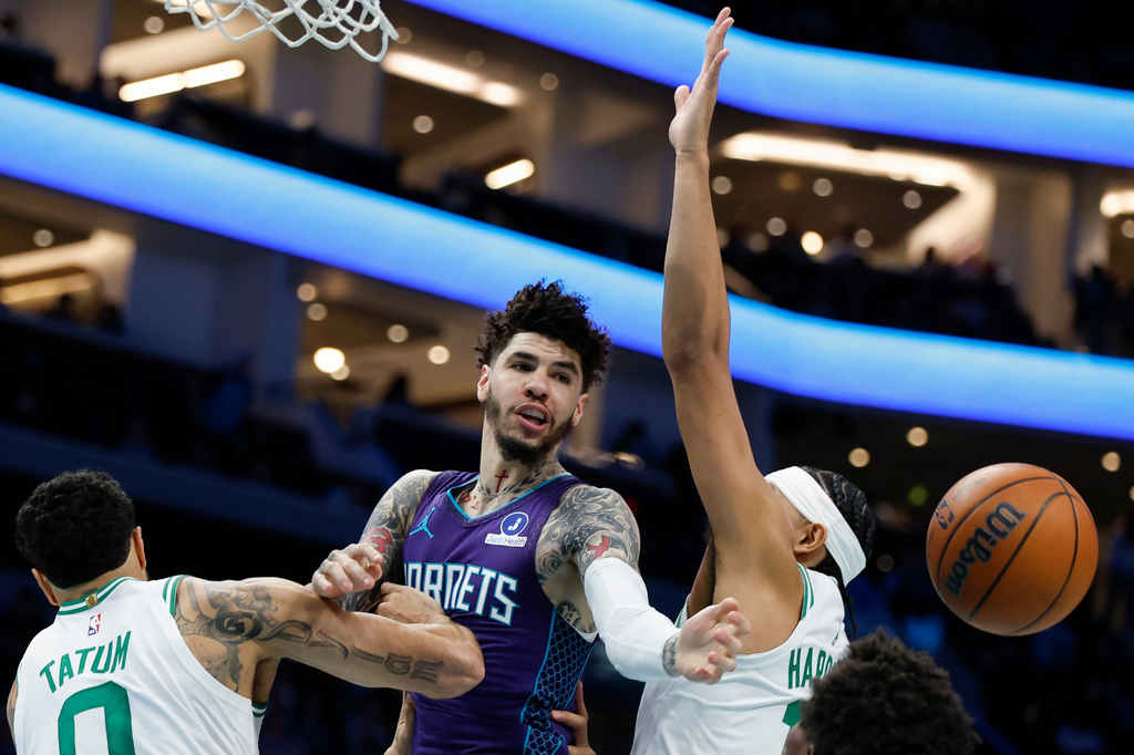 Charlotte Hornets guard LaMelo Ball, center, passes between Boston Celtics forward Jayson Tatum (0) and guard Ron Harper Jr. during the first half of an NBA basketball game in Charlotte, N.C., Sunday, March 29, 2026. (AP Photo/Nell Redmond)