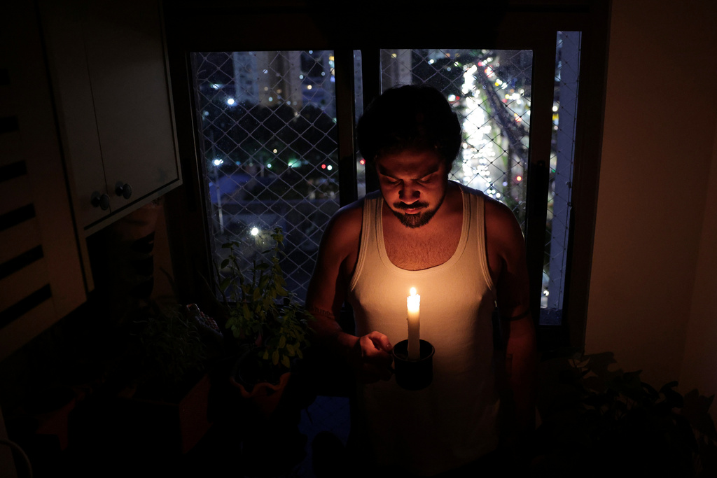 Gustavo Stancial holds a candle in his home during a blackout in Sao Paulo, Thursday, Dec. 11, 2025. (AP Photo/Ettore Chiereguini)