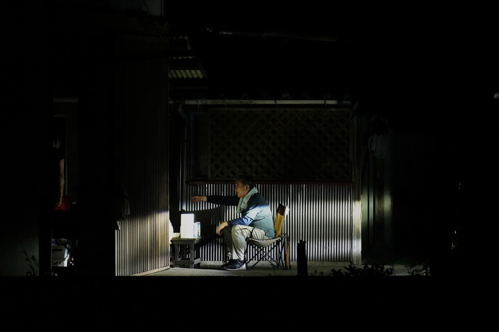 A man has meal under a car's headlights outside their home after they lost electricity in Yatsushiro, southern Japan, Thursday, July 30, 2026, two days after an earthquake hit the area. (AP Photo/Hiro Komae)
