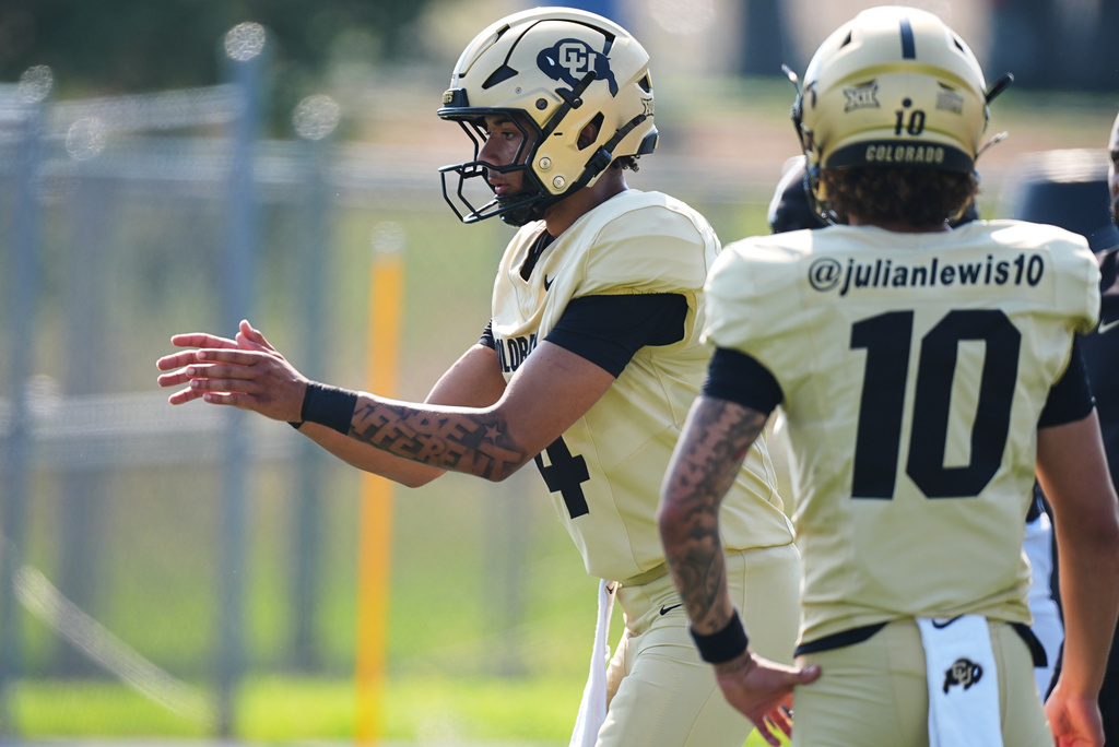 Colorado quarterback Kaneal Sweetwyne, back, fields a snap as quarterback Julian Lewis looks on during a practice at an NCAA college football training camp in Fountain, Colo., Thursday, Aug. 6, 2026. (AP Photo/David Zalubowski)