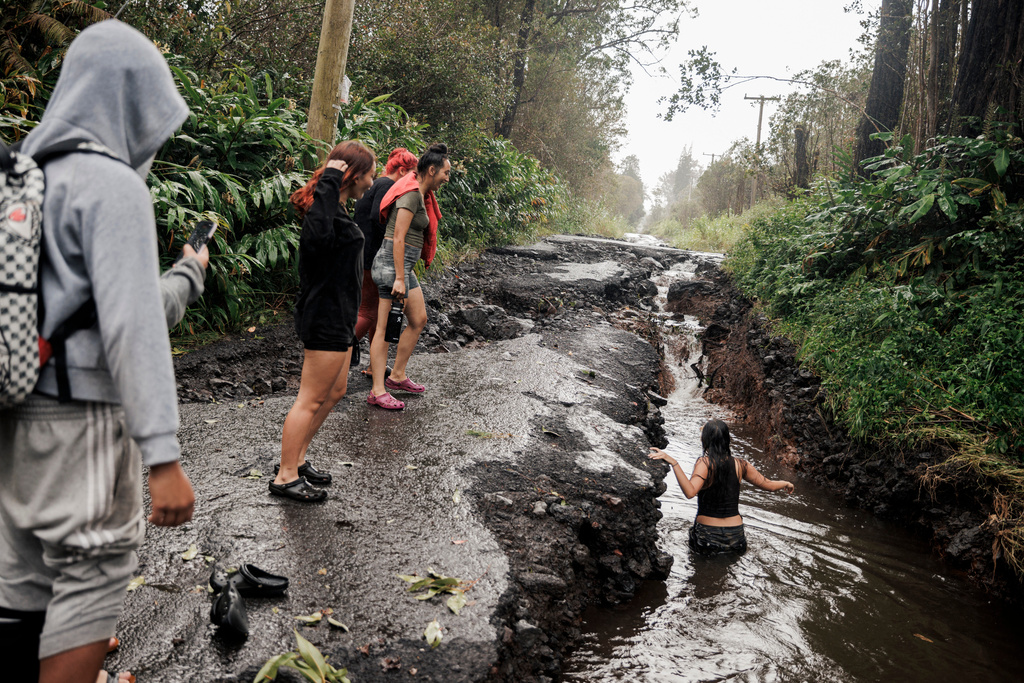 A teenager wades through a pool of water in a washed-out section of a damaged road in Mountain View, Hawaii, Sunday, Aug. 16, 2026, after a severe weather system went through the area. (Stephen Lam/San Francisco Chronicle via AP)
