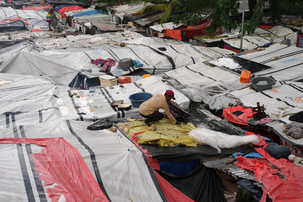 A man places plastic tarps over tents at a shelter for families displaced by gang violence during a break in the rain brought by Hurricane Melissa in Port-au-Prince, Haiti, Wednesday, Oct. 29, 2025. (AP Photo/Odelyn Joseph)