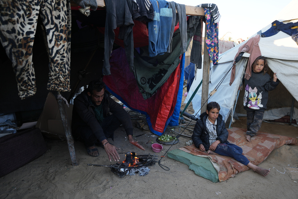 Displaced Palestinian Amr Al-Manaya, 35, sits by the fire with his children, Muhammad and Hala, next to their tent in Deir al-Balah, Gaza Strip, Saturday, Jan. 17, 2026. (AP Photo/Abdel Kareem Hana)
