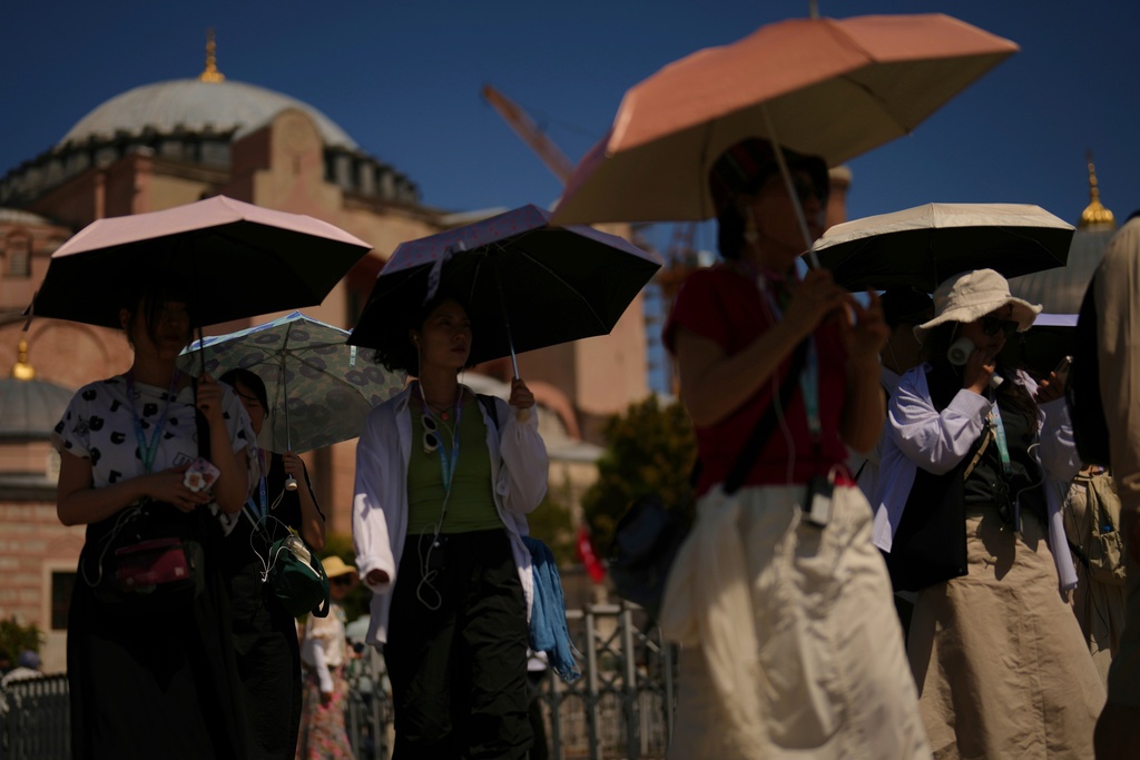 FILE - Tourists use umbrellas to shelter against the sun outside Hagia Sophia mosque during a hot summer day in Istanbul, Aug. 12, 2025. (AP Photo/Francisco Seco, File)