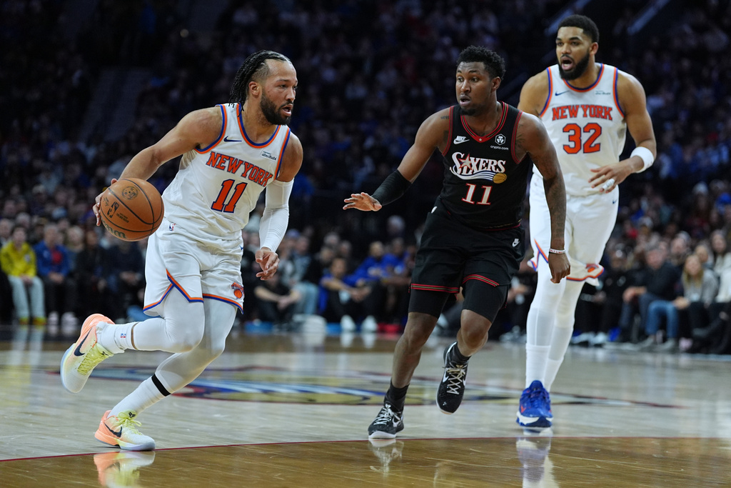 New York Knicks' Jalen Brunson (11) tries to get a shot past Philadelphia 76ers' Justin Edwards, center, during the first half of an NBA basketball game, Wednesday, Feb. 11, 2026, in Philadelphia. (AP Photo/Matt Rourke)
