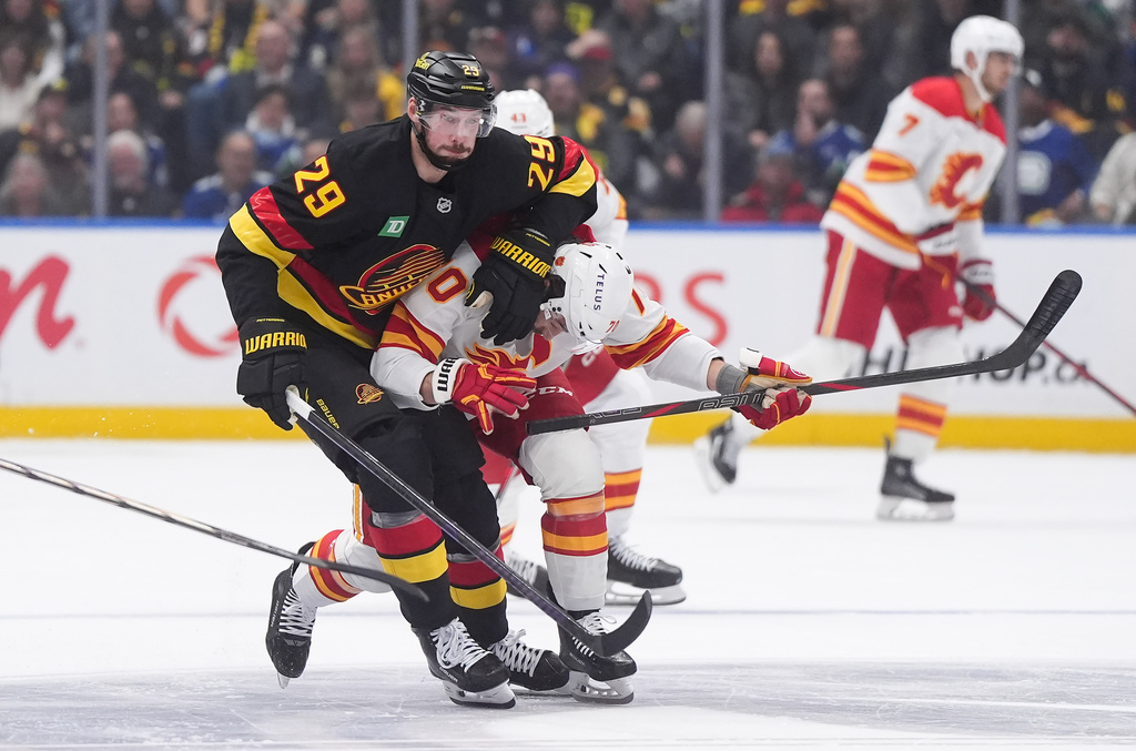 Vancouver Canucks' Marcus Pettersson, left, checks Calgary Flames' Ryan Lomberg, front right, during the first period of an NHL hockey game in Vancouver, British Columbia, Thursday, Oct. 9, 2025. (Darryl Dyck/The Canadian Press via AP)