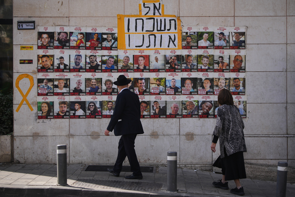 People look at photos of hostages held by Hamas in Gaza, in Jerusalem, Saturday, Oct. 4, 2025. Hebrew sign reads, "don't forget us". (AP Photo/Ohad Zwigenberg)