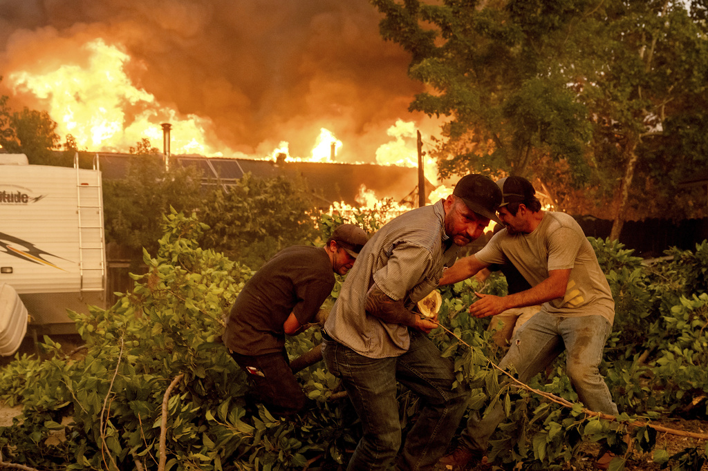 Residents work to stop flames from a burning home from spreading to a neighboring house as the 6-5 Fire burns through the Chinese Camp community of Tuolumne County, Calif., on Tuesday, Sept. 2, 2025. (AP Photo/Noah Berger)