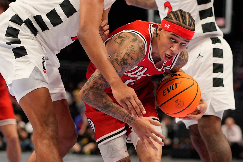 Utah guard Terrence Brown, center, gets past a pair of Cincinnati defenders during the first half of an NCAA college basketball game at the Big 12 Conference tournament Tuesday, March 10, 2026, in Kansas City, Mo. (AP Photo/Charlie Riedel)
