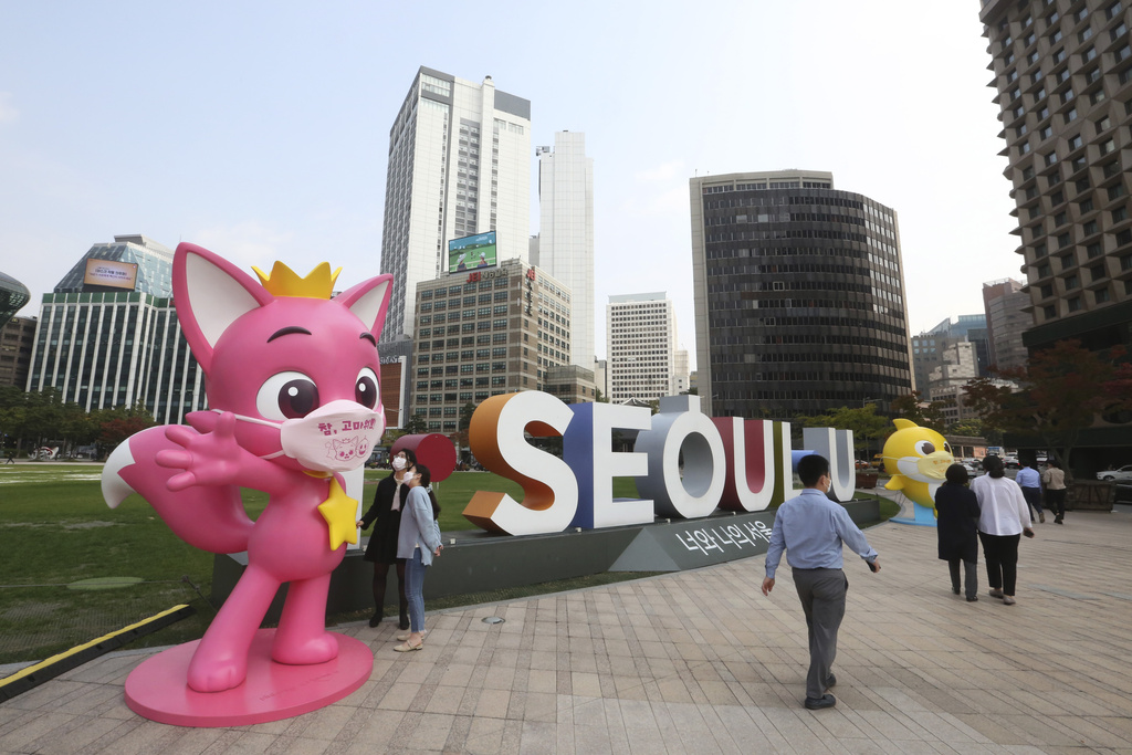 FILE - People walk near Pinkfong characters, from the South Korean kids’ content company, during a coronavirus prevention campaign at City Hall Plaza in Seoul, on Oct. 12, 2020. The writing on the character’s mask reads, “Thank you so much.” (AP Photo/Ahn Young-joon, File)