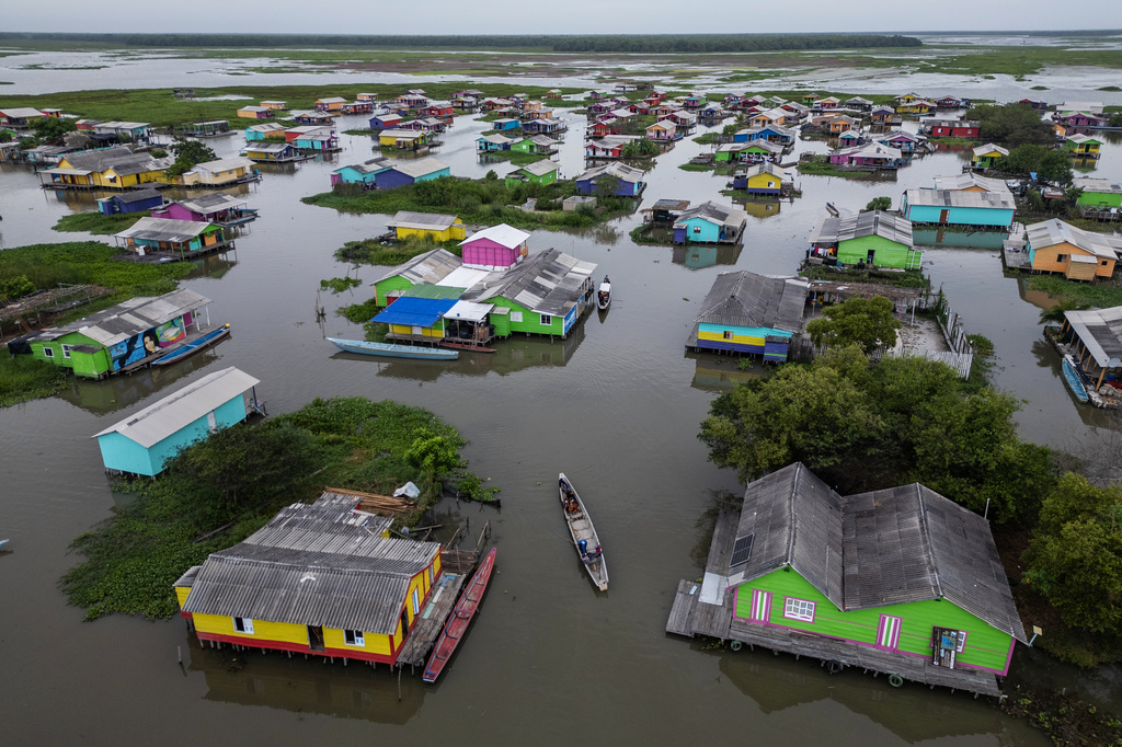 A boat navigates between homes surrounded by an invasive plant called a water hyacinth, also known as Eichhornia crassipes, in Nueva Venecia, Colombia, Thursday, April 30, 2026. (AP Photo/Ivan Valencia)