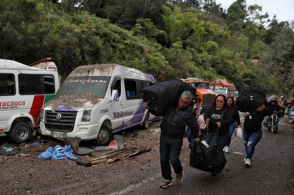 Travelers walk past vehicles damaged in an attack on the Pan-American Highway in Cajibio, Colombia, Sunday, April 26, 2026, where at least a dozen people were killed in an attack authorities blamed on dissident groups of the former FARC rebels. (AP Photo/Santiago Saldarriaga)