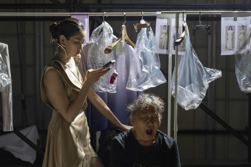A wardrobe assistant yawns as a model uses her phone as they wait backstage before the Misuity SS2026 China Fashion Week opening show on the outskirts of Beijing, China, Friday, Sept. 5, 2025. (AP Photo/Ng Han Guan)