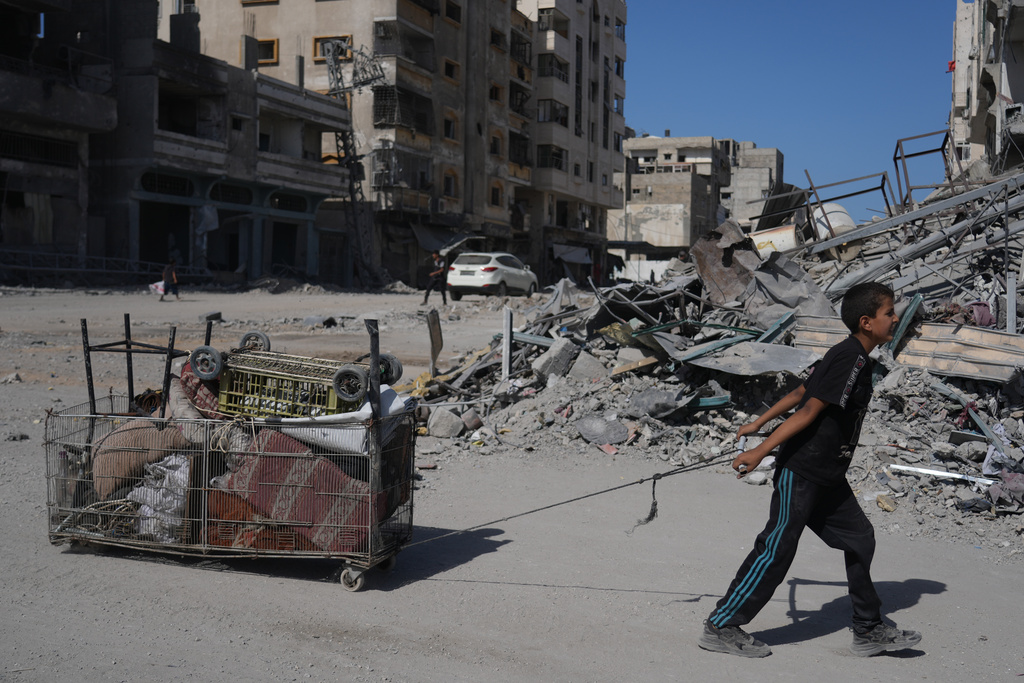 A displaced Palestinian boy pulls a cart loaded with belongings as he walks along the heavily damaged Al-Jalaa Street in Gaza City, Saturday, Oct. 11, 2025, after Israel and Hamas agreed to a pause in their war and the release of the remaining hostages. (AP Photo/Abdel Kareem Hana)