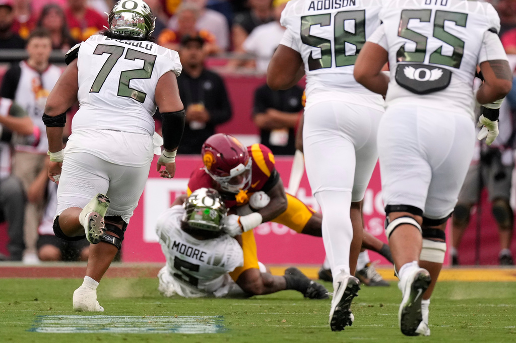 Oregon quarterback Dante Moore, center bottom, takes a hard tackle by lSouthern California inebacker Desman Stephens II, center top, during the first half of an NCAA college football game, Saturday, Sept. 26, 2026, in Los Angeles. (AP Photo/Mark J. Terrill)