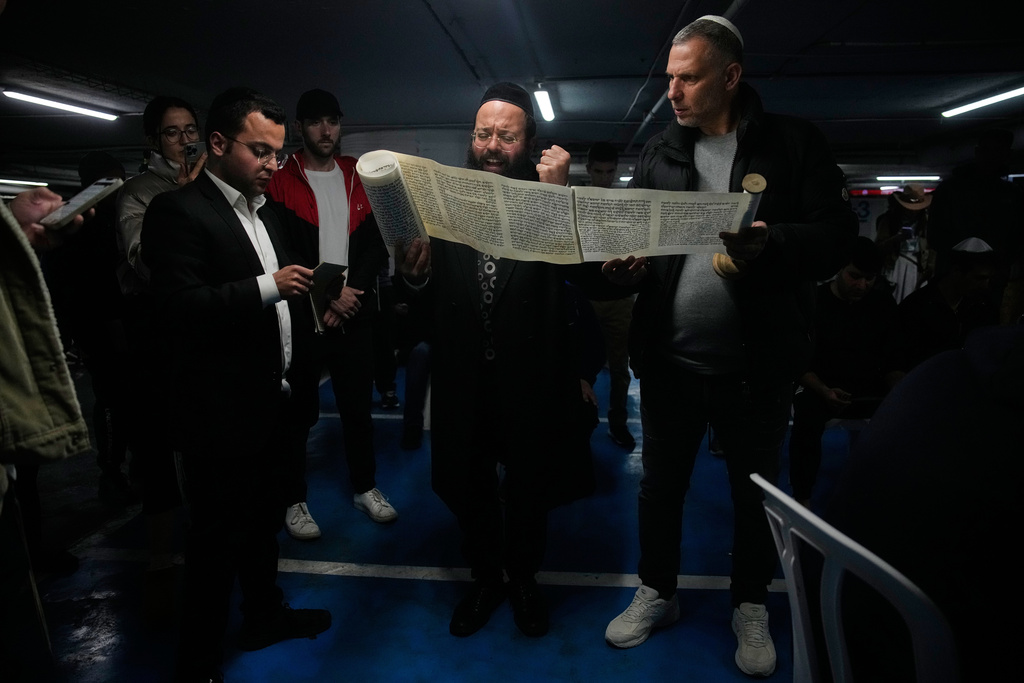 Jewish men read the Scroll of Esther as they celebrate the holiday of Purim in an underground parking garage as a precaution against possible Iranian missile attacks, in Tel Aviv, Israel, Monday, March 2, 2026. (AP Photo/Ohad Zwigenberg)