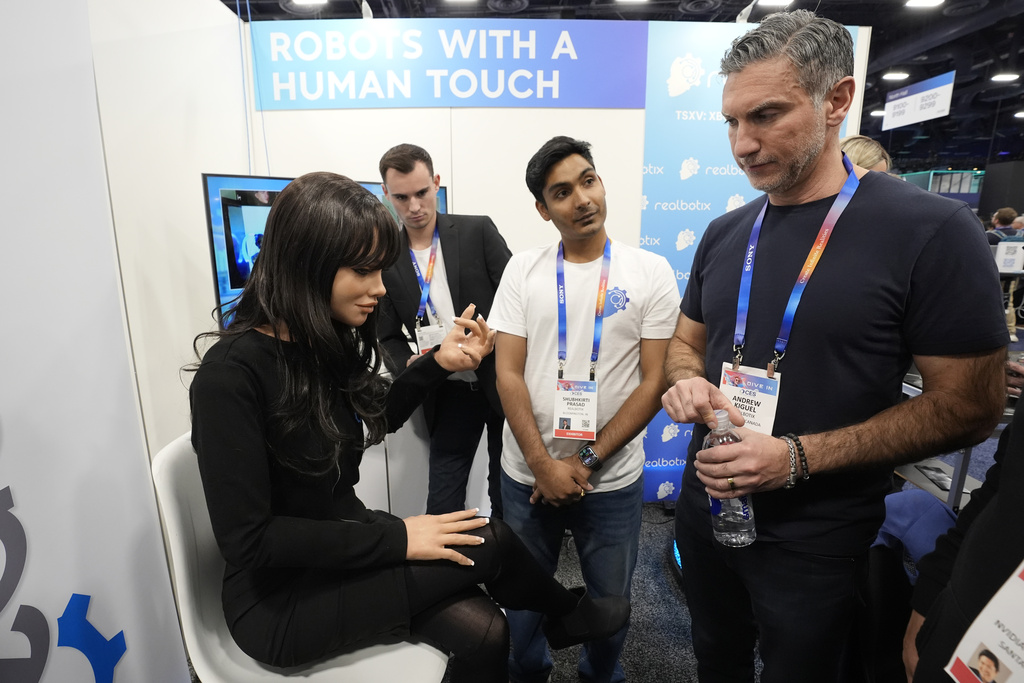 A Realbotix humanoid robot, left, speaks with attendees at a Realbotix booth during the CES tech show Wednesday, Jan. 8, 2025, in Las Vegas. (AP Photo/Abbie Parr)