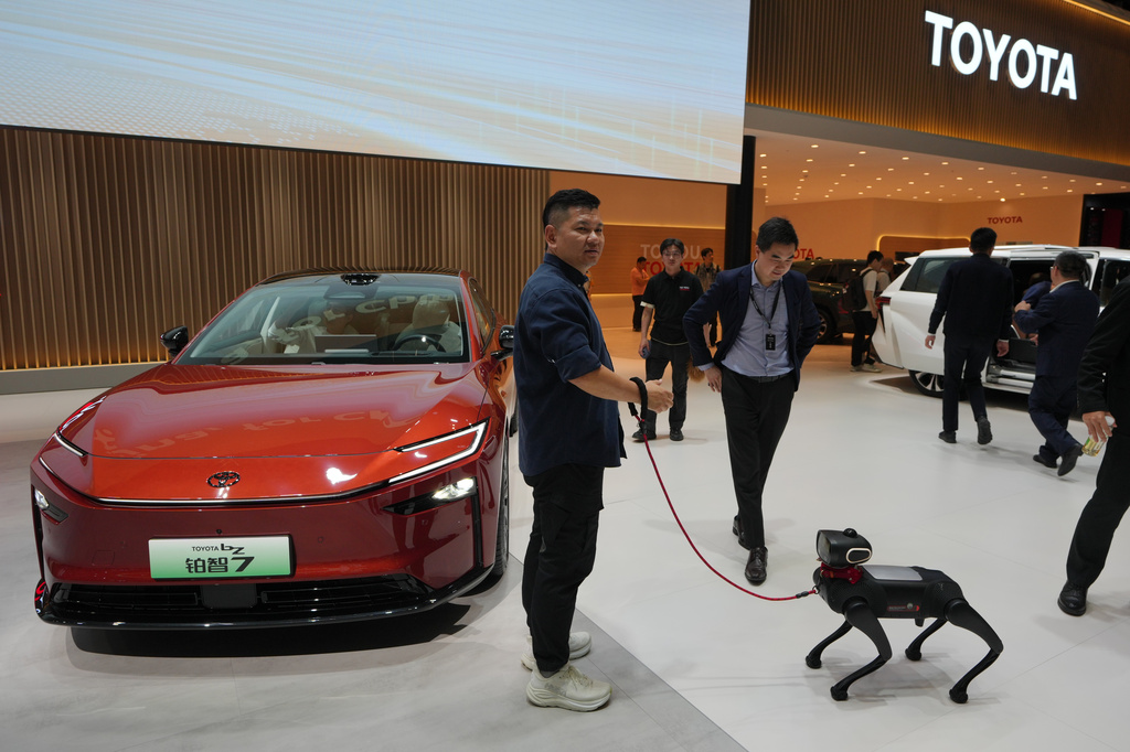 A visitor and his robotic dog stand near to the Toyota BZ7 EV model showcased at the Auto China 2026, in Beijing, Friday, April 24, 2026. (AP Photo/Andy Wong)