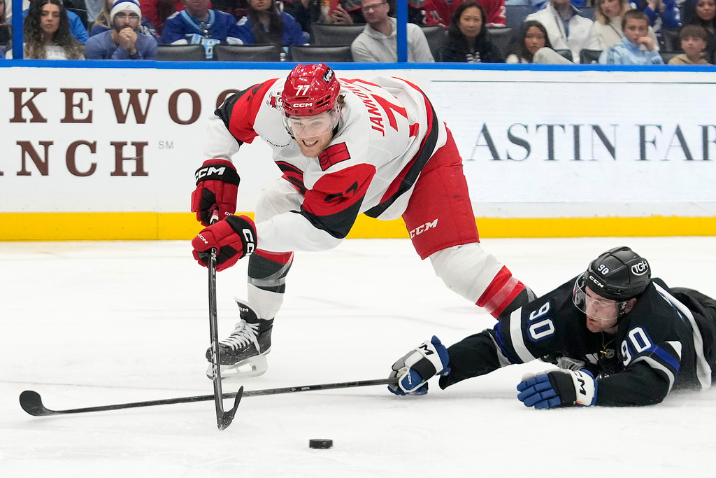 Tampa Bay Lightning defenseman J.J. Moser (90) kncoks the puck away from Carolina Hurricanes left wing Mark Jankowski during the third period of an NHL hockey game Saturday, Dec. 20, 2025, in Tampa, Fla. (AP Photo/Chris O'Meara)