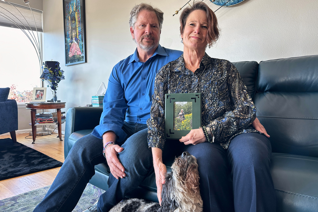 In this photo taken with a smartphone, Ken Parker and Carol Normandin pose for a portrait with their dog, Trooper, and a photo of their late daughter, Emily Normandin-Parker, in Seattle on Friday, Sept. 18, 2026. (AP Photo/Manuel Valdes)