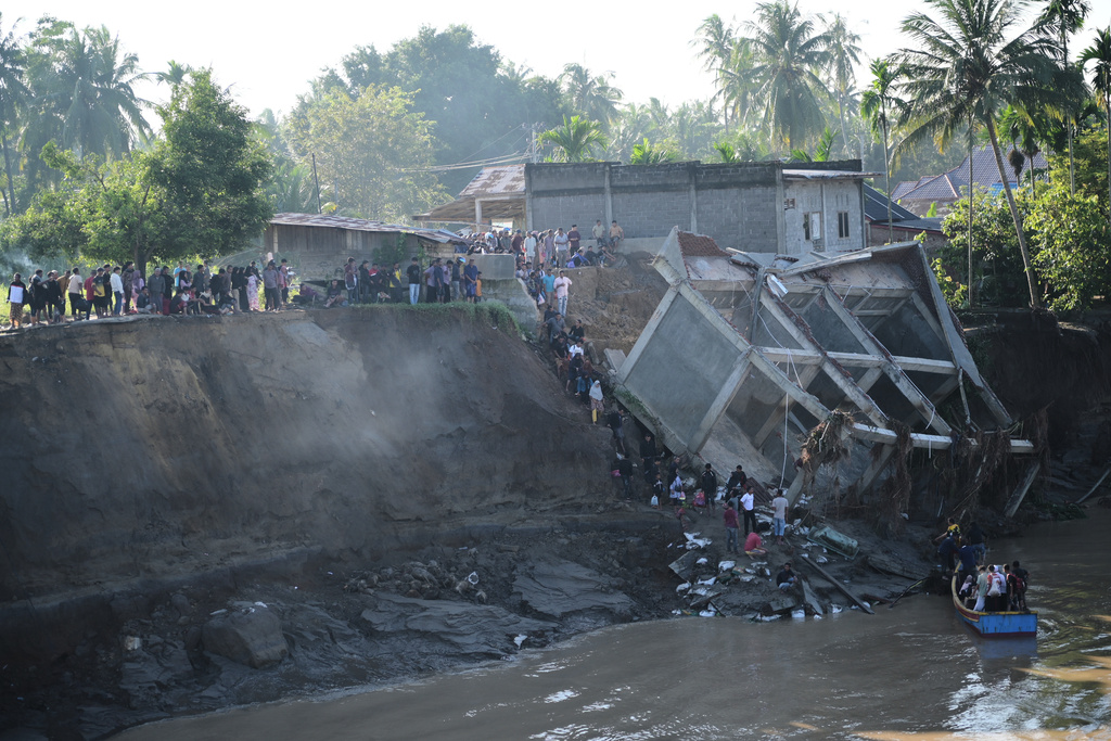 People walk down the embankment of a river to take a boat ride across after a bridge nearby collapsed during a flood in Bireun, Aceh province, Indonesia, Saturday, Nov. 29, 2025. (AP Photo/Reza Saifullah)