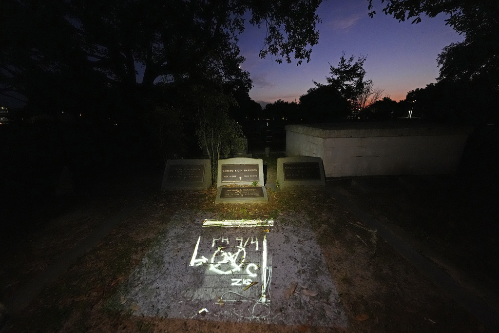 This photo of the FEMA markings indicating a deceased victim in the home of Michael Harrison, who died inside during Hurricane Katrina in Bay St. Louis, Miss., taken by AP photographer Gerald Herbert, nephew of Harrison, is projected Tuesday, Aug. 26, 2025, onto his grave in Pass Christian, Miss. (AP Photo/Gerald Herbert)