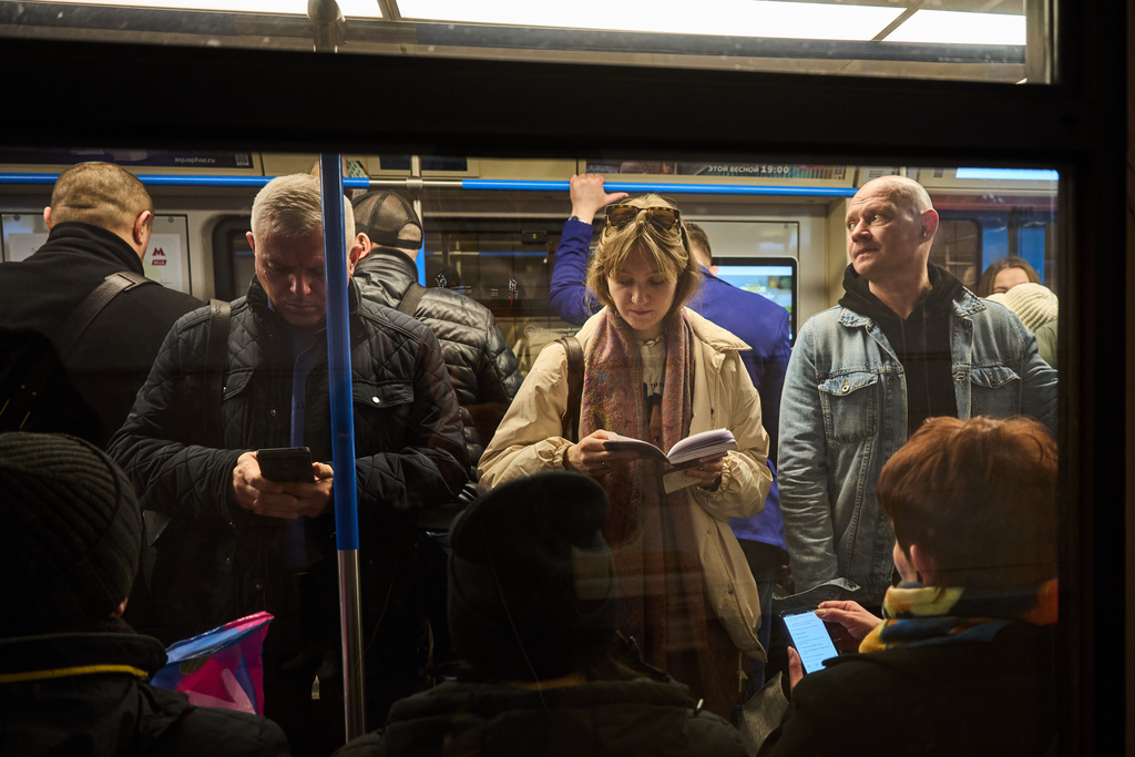 A man looks at his smartphone as a woman reads a book while on the subway in Moscow Thursday, March 12, 2026. (AP Photo/Alexander Zemlianichenko)