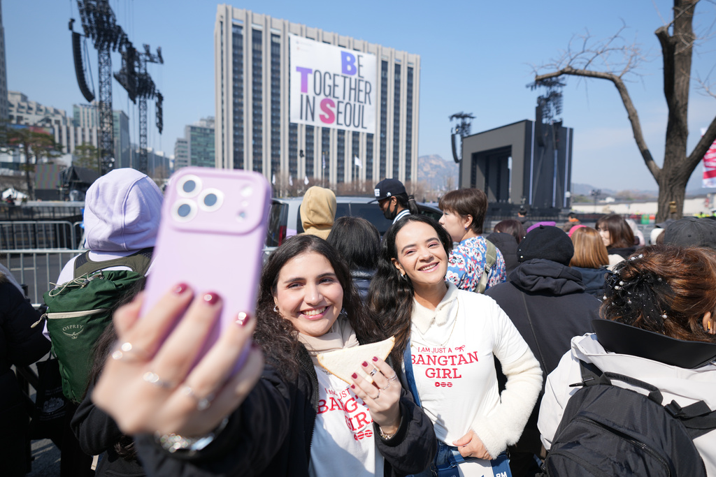 Fans of K-pop band BTS, Taylis Fahel, left, and Daniele Favero, right, from Brazil, take a selfie near a stage for the comeback concert of K-pop band BTS at Gwanghwamun Square in Seoul, South Korea, Saturday, March 21, 2026. (AP Photo/Lee Jin-man)