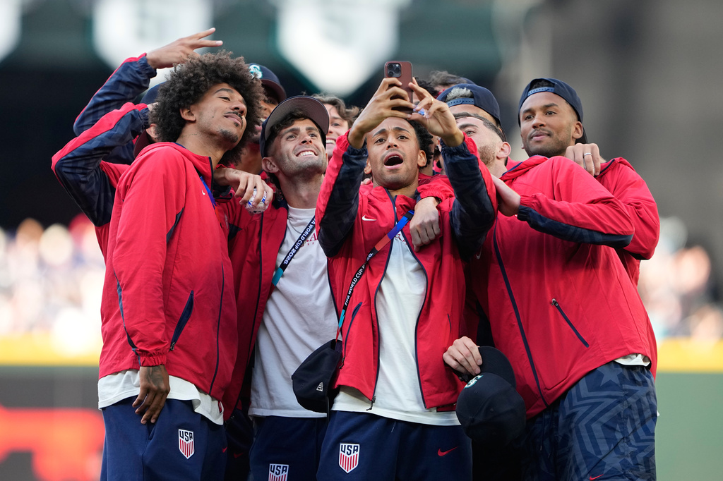 From left, United States men's national soccer team players Chris Richards, Christian Pulisic, Tyler Adams and Matt Turner take a photo with teammates on the field before a baseball game between the Seattle Mariners and the Toronto Blue Jays, Friday, July 3, 2026, in Seattle. (AP Photo/Lindsey Wasson)
