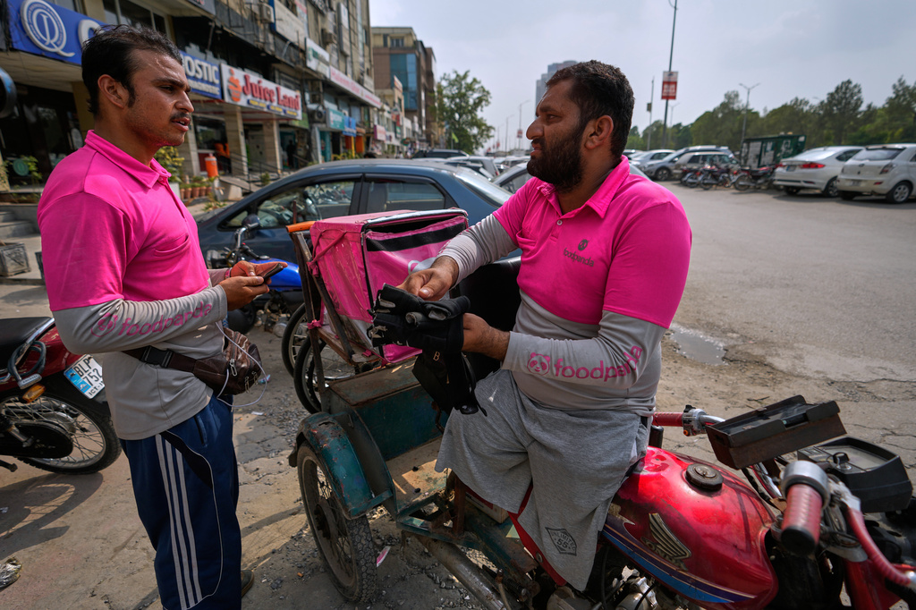 Hamza Ali, 28, who lost both legs in a road accident, speaks with a colleague as he leaves for a delivery order in Islamabad, Pakistan, Friday, July 17, 2026. (AP Photo/Anjum Naveed)