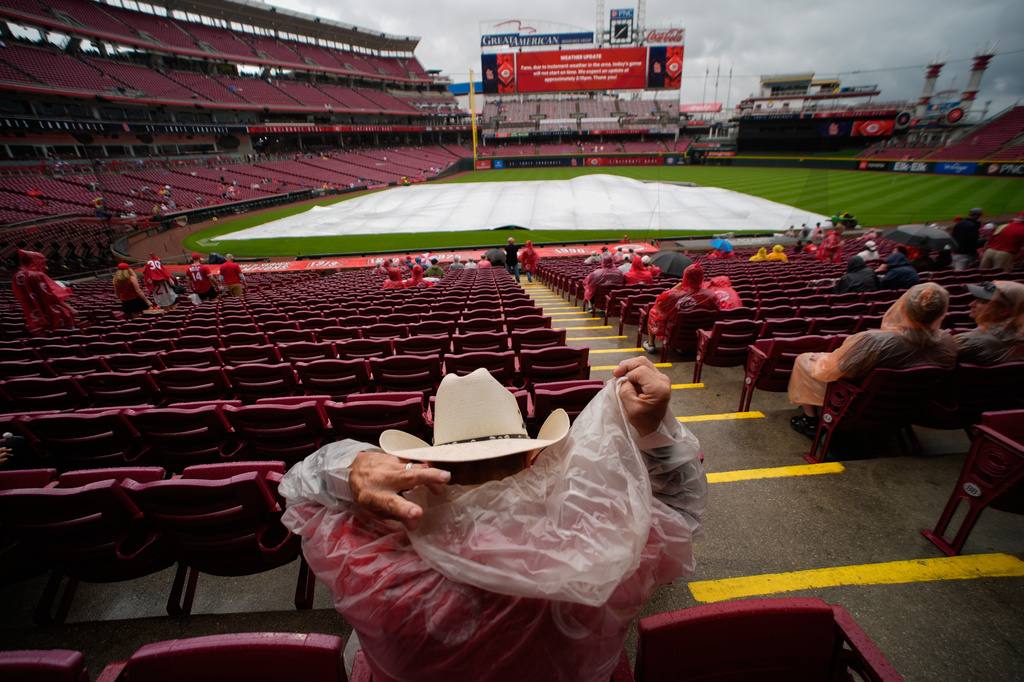 Cincinnati Reds fan Robert Plescher, foreground, from Texas, covers his cowboy hat with a rain poncho hood in the stands during a rain delay of a baseball game between the Reds and the St. Louis Cardinals before it was postponed in Cincinnati, Sunday, May 24, 2026. (AP Photo/Carolyn Kaster)