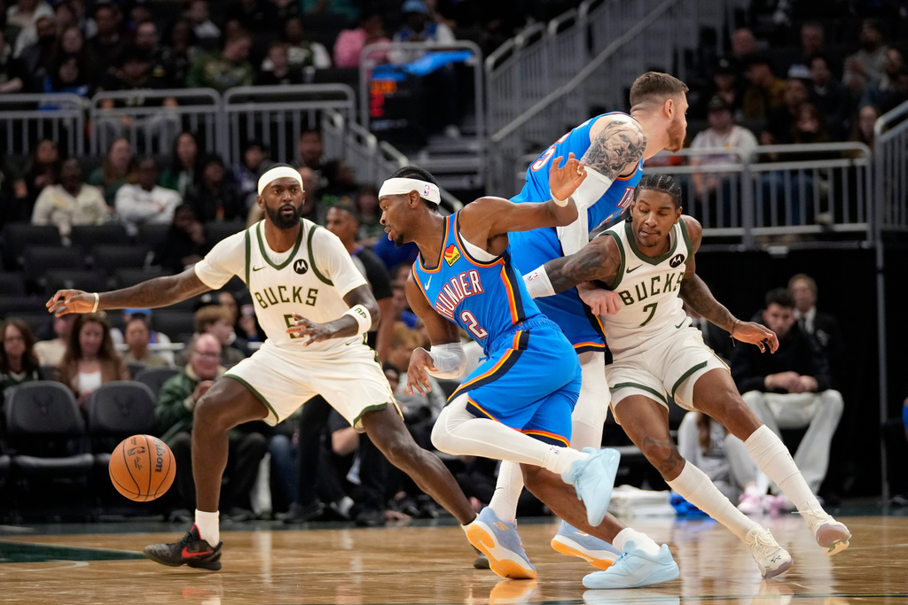 Milwaukee Bucks guard/forward Kevin Porter Jr. (7) attempts to get around Oklahoma City Thunder center Isaiah Hartenstein, second from right, as he trails behind Oklahoma City Thunder guard Shai Gilgeous-Alexander (2) as Milwaukee Bucks forward Bobby Portis (9) looks on during the first half of a preseason NBA basketball game Tuesday, Oct. 14, 2025, in Milwaukee. (AP Photo/Kayla Wolf)