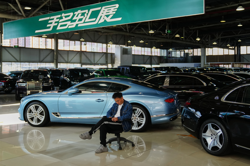 A man sits near luxury cars on offer at a second hand market in Beijing, Tuesday, Nov. 25, 2025. (AP Photo/Andy Wong)