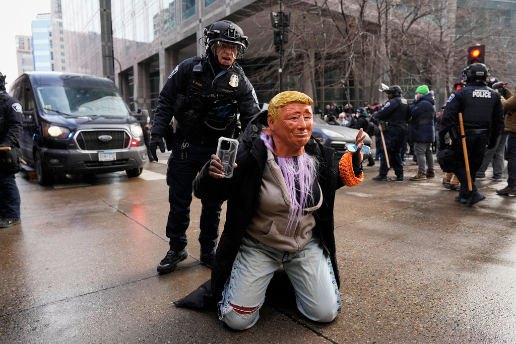 A person wearing a Trump mask is told to get up by a Minneapolis Police officer Saturday, Jan. 17, 2026, in Minneapolis. (AP Photo/Yuki Iwamura)