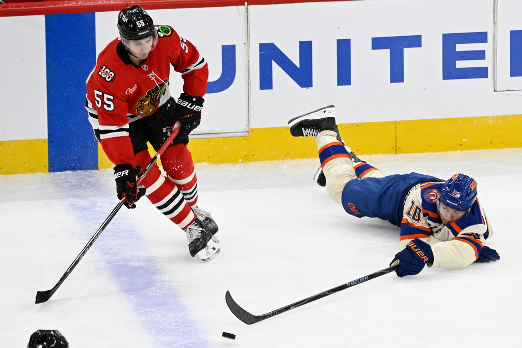 Edmonton Oilers center Curtis Lazar, right, flips the puck past Chicago Blackhawks defenseman Artyom Levshunov (55) during the second period of an NHL hockey game, Monday, Jan. 12, 2026, in Chicago. (AP Photo/Matt Marton)