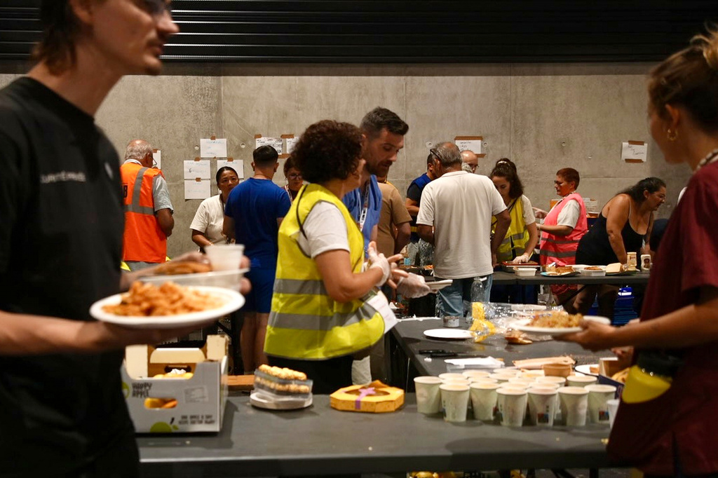 People collect food at a temporary shelter for those displaced by wildfires in Bordeaux, France, Tuesday, July 28, 2026. (AP Photo/Eva van Dam)