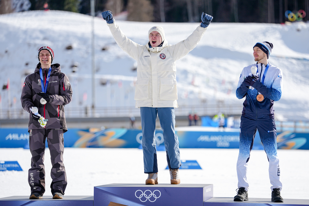 Gold medalist Jens Luraas Oftebro, of Norway, celebrates on the podium flanked by silver medalist Johannes Lamparter, of Austria, left, and bronze medalist Ilkka Herola, of Finland, after the nordic combined individual Gundersen large hill/10km at the 2026 Winter Olympics, in Tesero, Italy, Tuesday, Feb. 17, 2026. (AP Photo/Matthias Schrader)