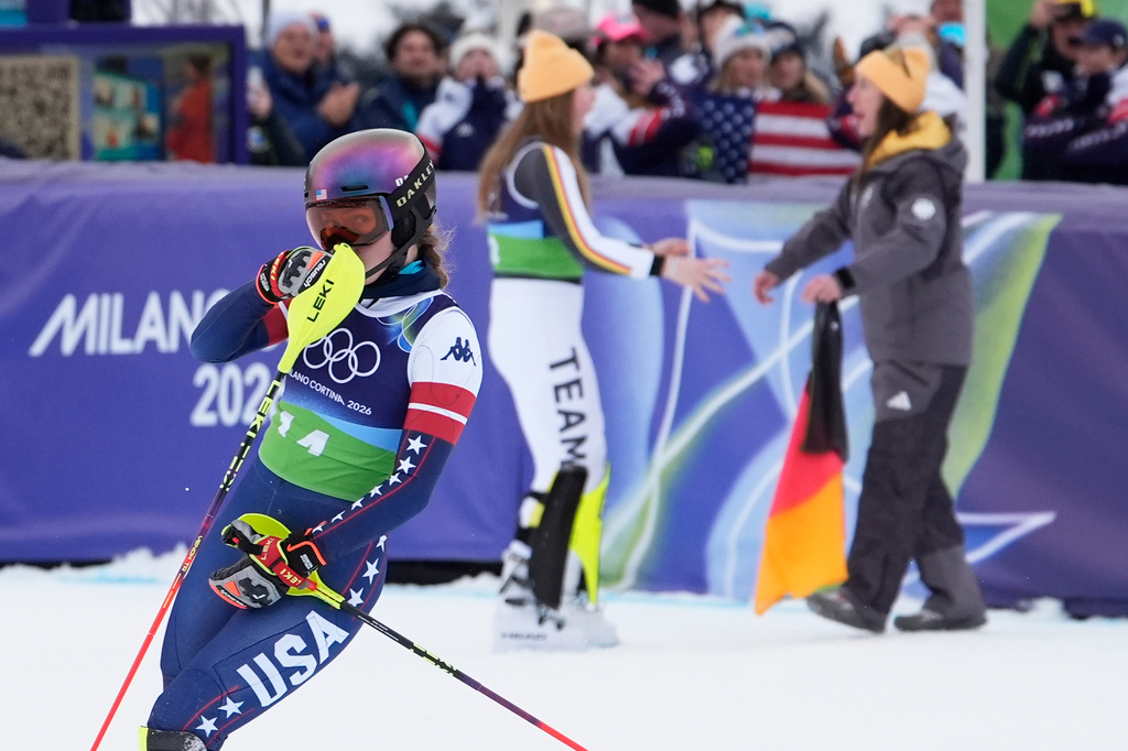 United State's Mikaela Shiffrin reacts as she looks back to see her disappointing time as Germany's Emma Aicher, background left, and Kira Weidle Winkelmann celebrate winning the silver medal in an alpine ski, women's team combined race, at the 2026 Winter Olympics, in Cortina d'Ampezzo, Italy, Tuesday, Feb. 10, 2026. (AP Photo/Robert F. Bukaty)
