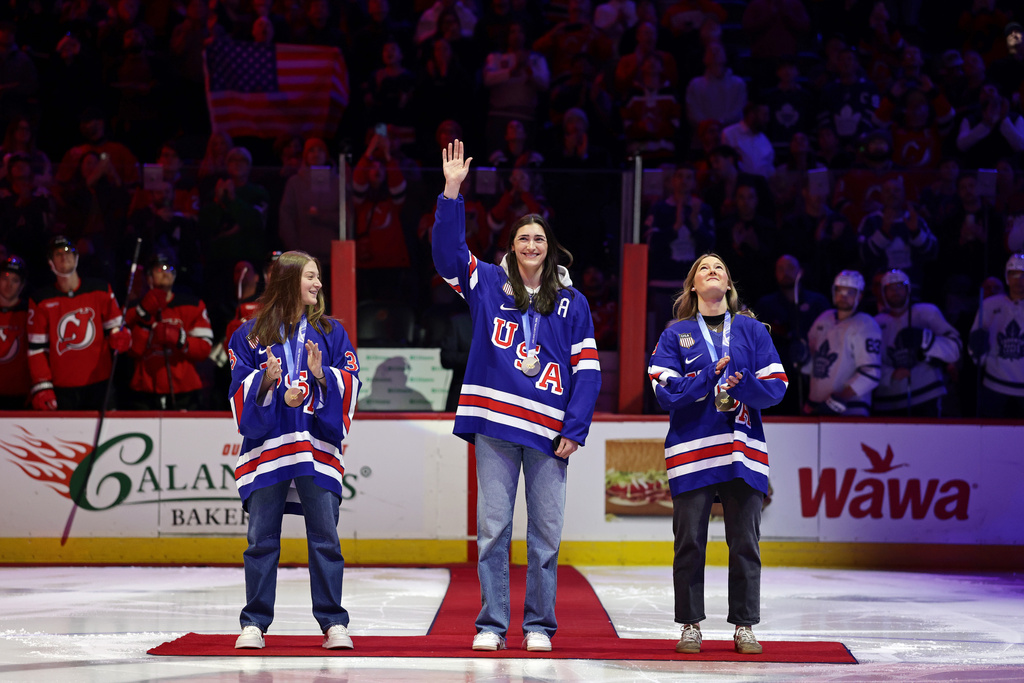 United States women's gold medal hockey players Megan Keller, center, Aerin Frankel, left, and Haley Winn, right, acknowledge the crowd before a ceremonial puck drop ahead of an NHL hockey game Wednesday, March 4, 2026, in Newark, N.J. (AP Photo/Adam Hunger)