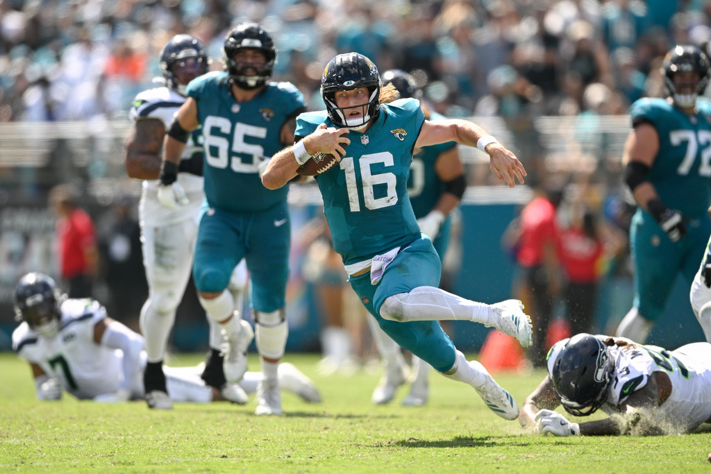 Jacksonville Jaguars quarterback Trevor Lawrence (16) is tripped up by Seattle Seahawks defensive end Leonard Williams, bottom right, after trying to get yardage during the first half of an NFL football game Sunday, Oct. 12 2025, in Jacksonville, Fla. (AP Photo/Phelan M. Ebenhack)