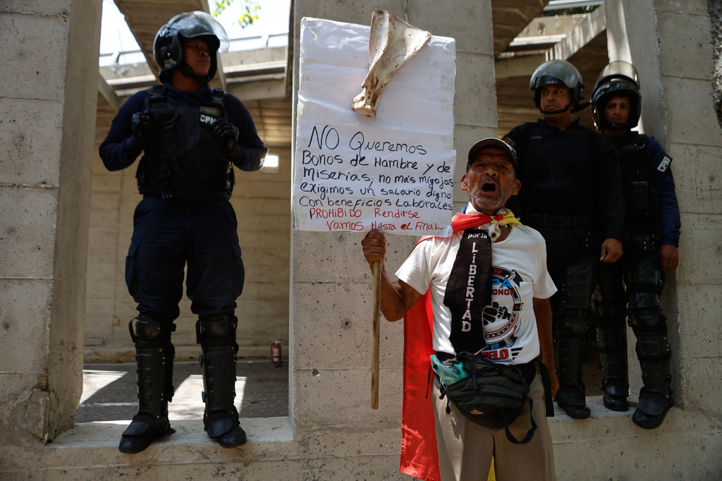 Bolivarian National Police flank a protester who is taking part in a march demanding higher salaries, pensions and benefits, in Caracas, Venezuela, Thursday, April 9, 2026. (AP Photo/Pedro Mattey)