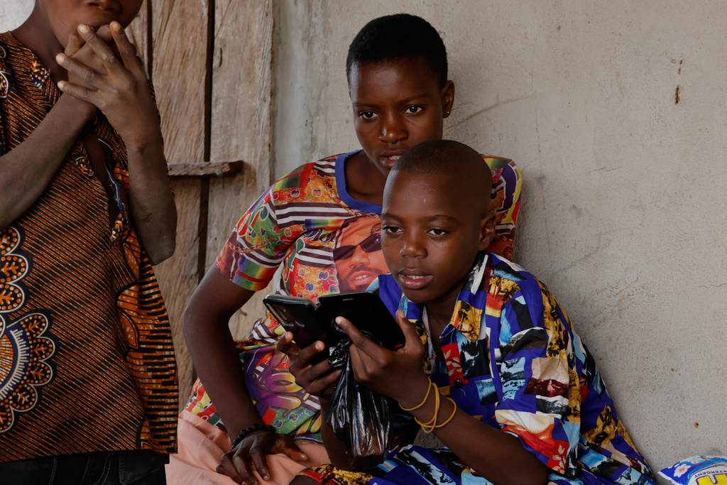 Onyeka Chieme, right, a student of St. Mary's Catholic School, who was abducted by gunmen and later released, checks a mobile phone in his house in Papiri, Nigeria, Wednesday, Dec. 10, 2025. (AP Photo/Afolabi Sotunde)