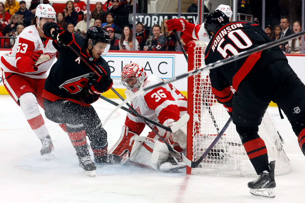 Carolina Hurricanes' Eric Robinson (50) stuffs the puck past Detroit Red Wings goaltender John Gibson (36) for a goal with teammate Sebastian Aho and Red Wings' Moritz Seider (53) nearby during the second period of an NHL hockey game in Raleigh, N.C., Saturday, Dec. 27, 2025. (AP Photo/Karl DeBlaker)