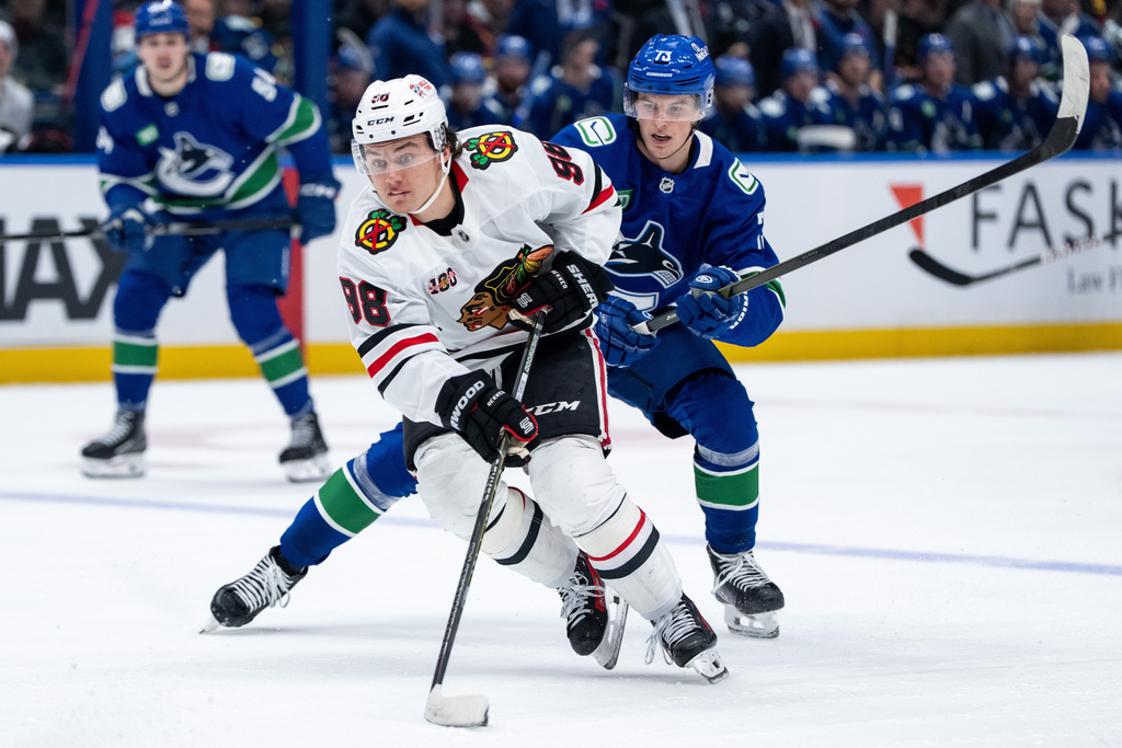 Chicago Blackhawks' Connor Bedard (98) and Vancouver Canucks' Lukas Reichel (73) vie for the puck during the second period of an NHL hockey game in Vancouver, on Wednesday, Nov. 5, 2025. (Ethan Cairns/The Canadian Press via AP)