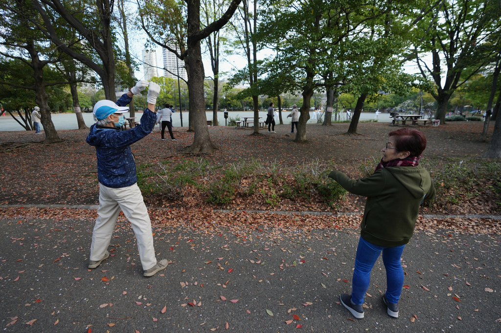 People perform a stretching exercise while listening to music and guidance from radio at a public park in Tokyo, Monday, April 6, 2026. (AP Photo/Hiro Komae)
