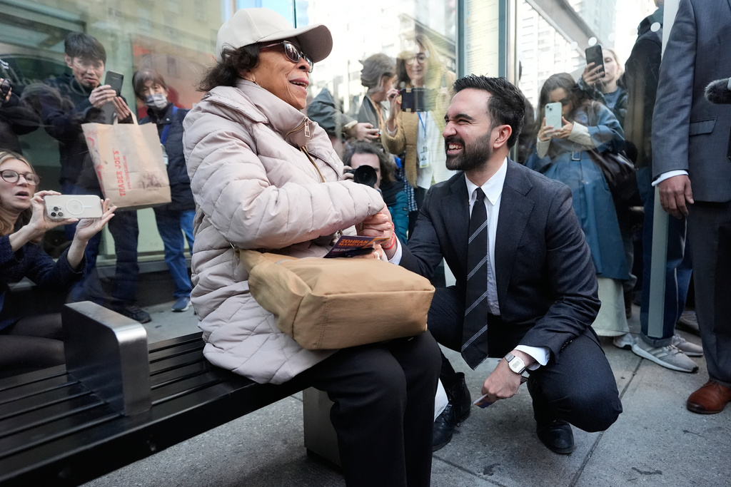 New York City mayoral candidate Zohran Mamdani talks with Rita Bellevue as she waits at a bus stop in New York, Monday, Oct. 27, 2025. (AP Photo/Seth Wenig)