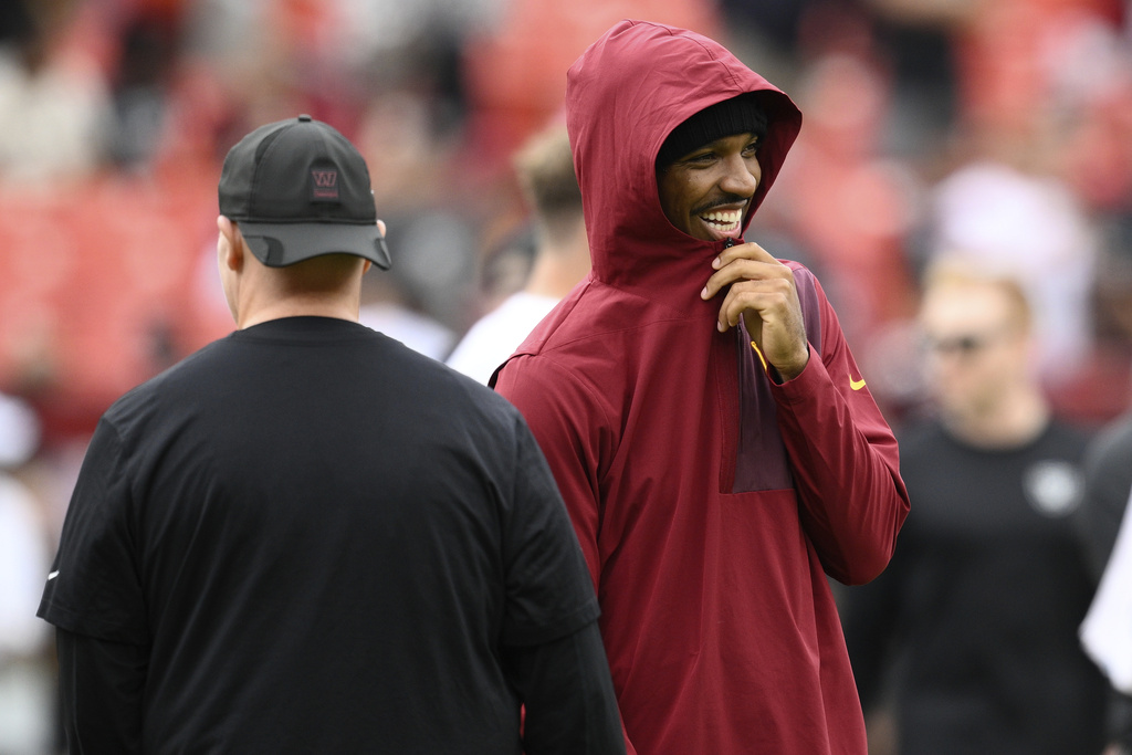 Washington Commanders quarterback Jayden Daniels, right, watches during warm ups before an NFL football game against the Las Vegas Raiders, Sunday, Sept. 21, 2025, in Landover, Md. (AP Photo/Nick Wass)
