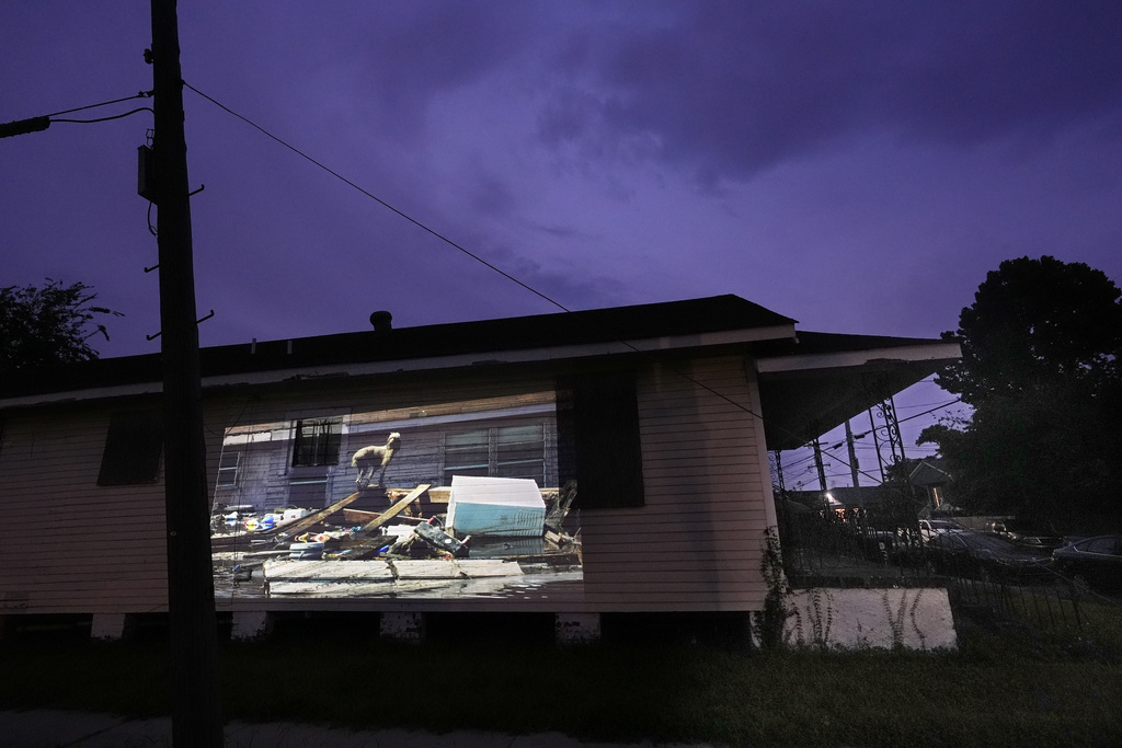 This photo of a poodle perching itself precariously upon a pile of trash while surrounded by floodwaters in the aftermath of Hurricane Katrina in New Orleans, taken by AP photographer Rick Bowmer, is projected Thursday, Aug. 21, 2025, onto a house in a neighborhood that was flooded by the storm. (AP Photo/Gerald Herbert)